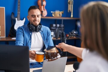 Man and woman musicians smiling confident drinking coffee at music studio