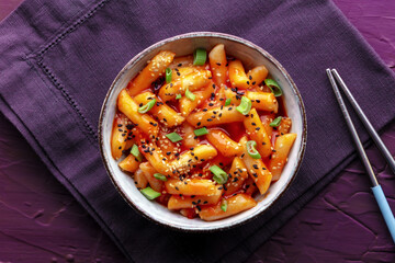 Tteokbokki or topokki, Korean street food, spicy rice cakes in red pepper gochujang sauce, overhead flat lay shot with chopsticks