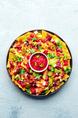 Loaded nachos. Mexican nacho chips with beef, guacamole sauce, cheese salsa, beans and peppers, on a slate background, overhead shot with a place for text