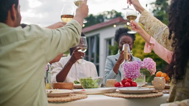 Celebration party dinner at home yard. Group of diverse multicultural people, friends drinking, making toast with white wine and have conversation together. Happiness and joyful wonderful moments.