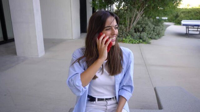Young female student sitting at university campus, using phone to send online messages when answers the cell phone smiling. Copy space.