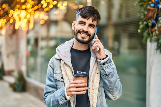 Young hispanic man talking on the smartphone drinking coffee at street