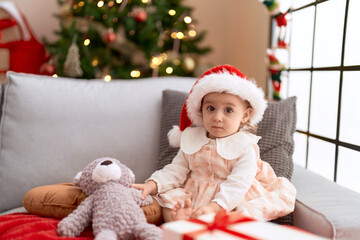 Obraz na płótnie Canvas Adorable caucasian girl sitting on sofa by christmas tree at home