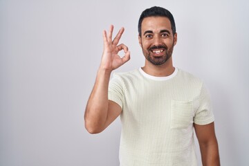Naklejka premium Hispanic man with beard standing over isolated background smiling positive doing ok sign with hand and fingers. successful expression.