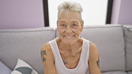 Grey-haired mature woman resting easy on comfortable sofa at home, confident expression radiating...