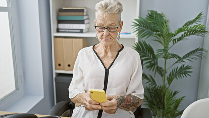 Elegant, grey-haired senior woman boss, concentrating at work, seriously typing messages on...
