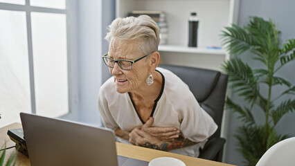 Stressed, overworked grey-haired senior business woman suffers heart attack at work in office,...