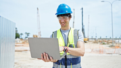 Young hispanic man architect smiling confident using laptop at construction place