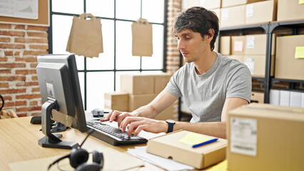 Young hispanic man ecommerce business worker typing on computer with serious face at office