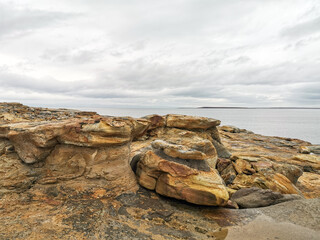 The shore of red stones next to the rocks are Two Brothers on the Fishing Peninsula. The picturesque shore of the harsh Barents Sea. The North of Russia. The Kola Peninsula. The Arctic