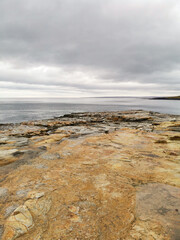 The shore of red stones next to the rocks are Two Brothers on the Fishing Peninsula. The picturesque shore of the harsh Barents Sea. The North of Russia. The Kola Peninsula. The Arctic
