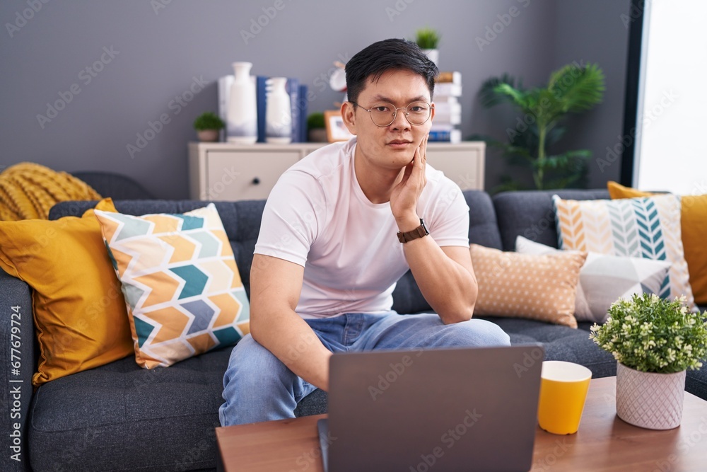 Sticker young asian man using laptop at home sitting on the sofa touching mouth with hand with painful expre