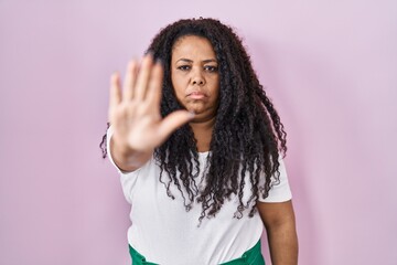 Plus size hispanic woman standing over pink background doing stop sing with palm of the hand. warning expression with negative and serious gesture on the face.
