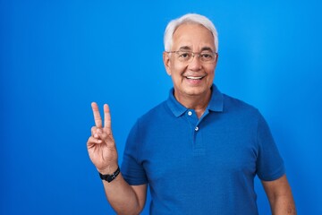 Middle age man with grey hair standing over blue background smiling with happy face winking at the...