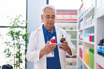 Middle age grey-haired man pharmacist smiling confident holding medication bottles at pharmacy