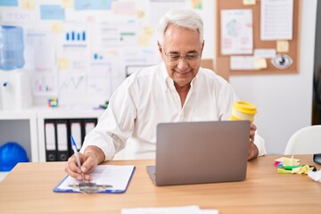 Middle age grey-haired man business worker using laptop writing on document at office