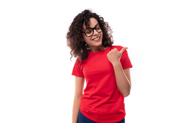 young smart pretty curly brunette woman dressed in a red t-shirt points with her hand to the advertising space