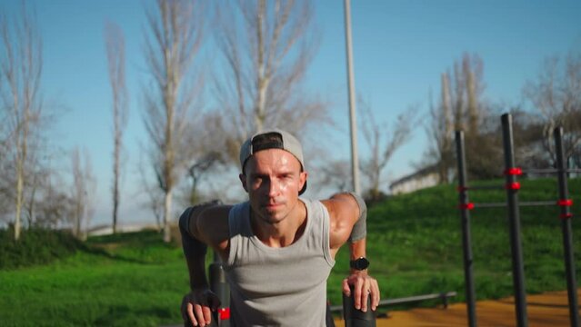 Man using parallel bars for triceps workout in outdoor setting. Athlete utilizing his body weight for resistance and support. Male body-weight arm exercise on parallel bars