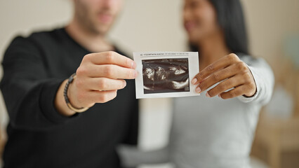 Beautiful couple sitting on bed holding baby ultrasound smiling at bedroom