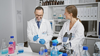 Fototapeta premium Inside the lab, two enthusiastic scientists in conversation, juggling their laptop and test tubes in an indoor laboratory