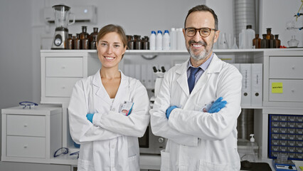 Two smiling scientists working together in lab, standing with arms crossed, marvelling at their medical breakthrough