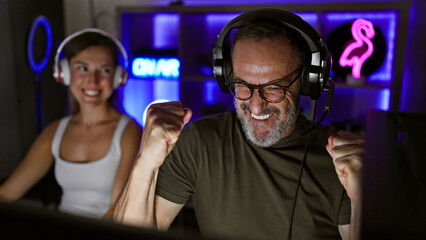 Exciting night in gaming room, two cheerful gamers, father and daughter, triumph together in epic video game win, streaming their victory with headsets and smiles © Krakenimages.com