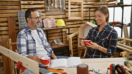 Man and woman carpenters, cheers to carpentry! drinking coffee and sharing laughs in their cozy timber-filled workplace