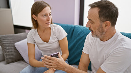 At home, father and daughter in a heated argument over smartphone usage, sitting unhappily on the...
