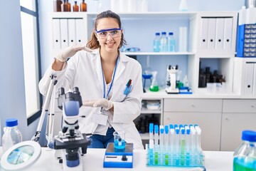 Young hispanic woman working at scientist laboratory gesturing with hands showing big and large size sign, measure symbol. smiling looking at the camera. measuring concept.
