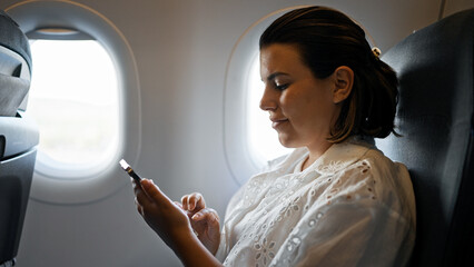Beautiful young hispanic woman using smartphone on the plane