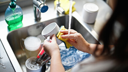 Young beautiful hispanic woman washing plates at the kitchen