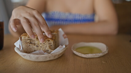 Young hispanic woman dipping bread into olive oil at the restaurant
