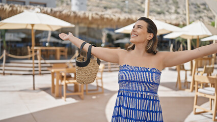 Young hispanic woman smiling happy with open arms at sunny restaurant terrace