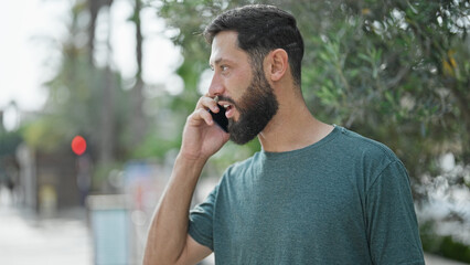 Young hispanic man talking on smartphone with serious expression at park