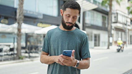 Young hispanic man using smartphone and earphones at street