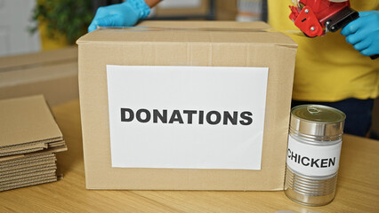 Young hispanic man volunteer packing cardboard box to donate at charity center