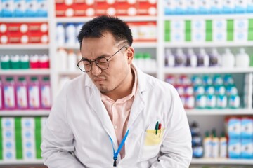 Chinese young man working at pharmacy drugstore with hand on stomach because indigestion, painful illness feeling unwell. ache concept.