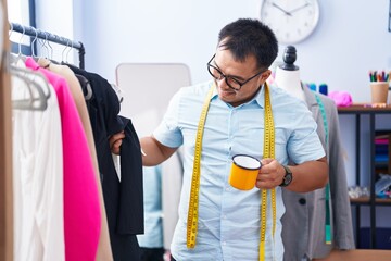 Young chinese man tailor smiling confident drinking coffee at tailor shop