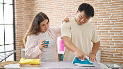 Man and woman couple ironing clothes drinking coffee at laundry room