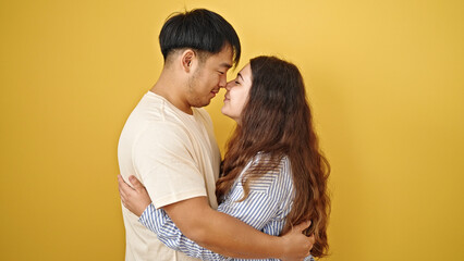 Man and woman couple hugging each other touching nose over isolated yellow background