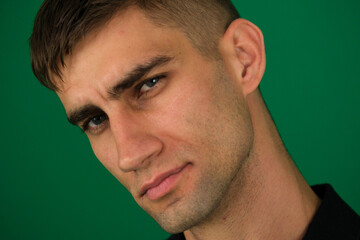 Fototapeta premium emotions of a handsome man guy on a green background chromakey close-up dark hair young man. Headshot of thoughtful handsome man, looking intrigued and squinting, thinking about something,