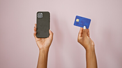 African american woman holding smartphone and credit card over isolated pink background