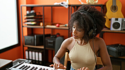 African american woman musician wearing headphones playing piano at music studio