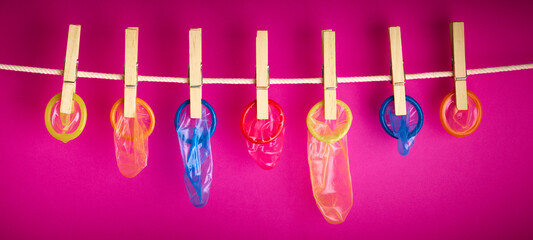 condoms hanging on a rope over pink background