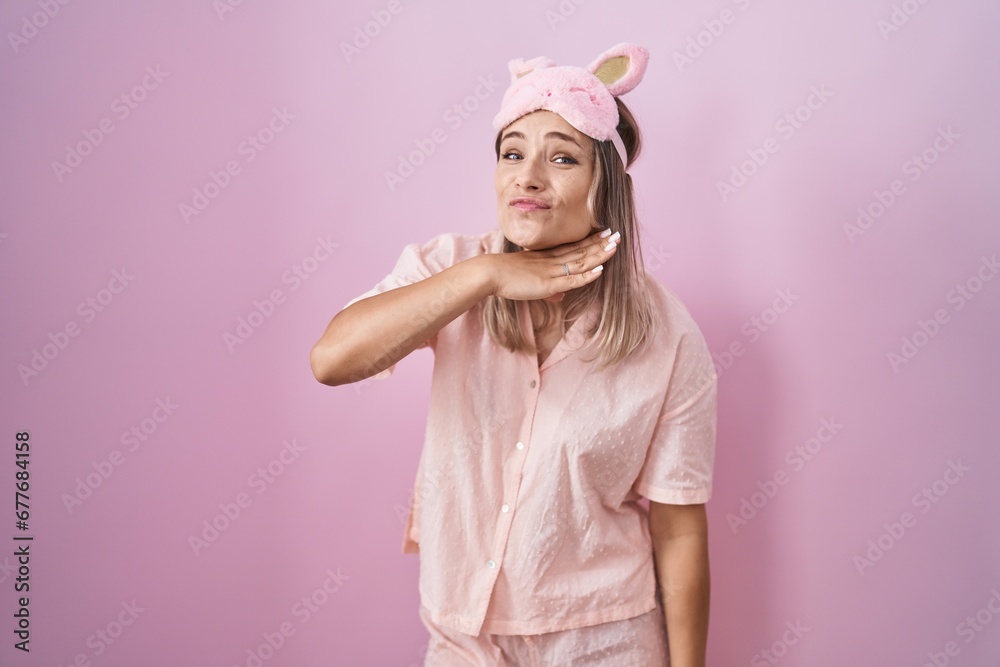 Canvas Prints Blonde caucasian woman wearing sleep mask and pajama cutting throat with hand as knife, threaten aggression with furious violence