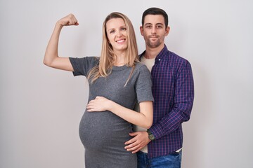 Young couple expecting a baby standing over white background strong person showing arm muscle,...
