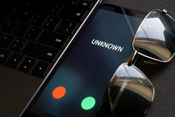 Smartphone with an unknown and unidentified incoming call next to laptop and black glasses....
