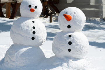Obraz premium figures made of snow. large figurines of snowmen stand on a snowy road with a carrot instead of a nose and black mud eyes and buttons on the body