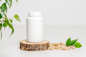 White bottle with herbal vitamins on wooden podium. Vitamins medical bottle mockup with pills and green leaves on white background, organic medication. Natural herbal supplement, healthy lifestyle.