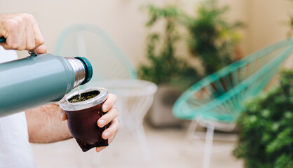 A man pours water from a thermos into a mate. Yerba Mate, traditional South American hot drink.Middle age latin american man enjoying outdoors. - obrazy, fototapety, plakaty
